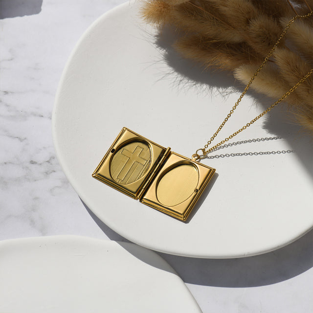 an opened gold Cross Photo Box Locket Necklace on a white disc