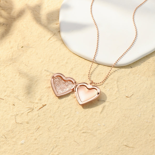 an opened rose gold Engraved Heart Locket Necklace on sand with flat white stone
