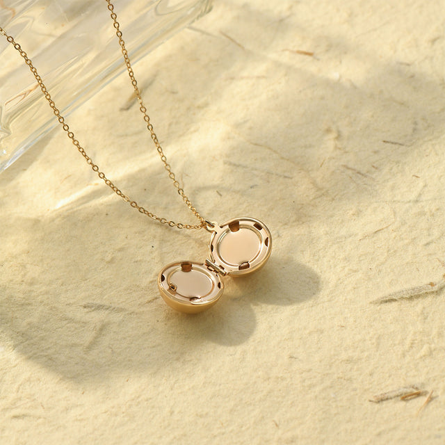 an opened gold Round Ball Locket Necklace on sand