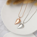 rose gold and silver colored Couple's Heart Locket Necklaces on a white circle disc
