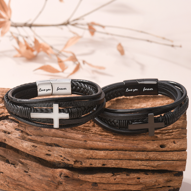 Lifestyle image of the silver and black variants of the leather cross bracelet on a piece of wood