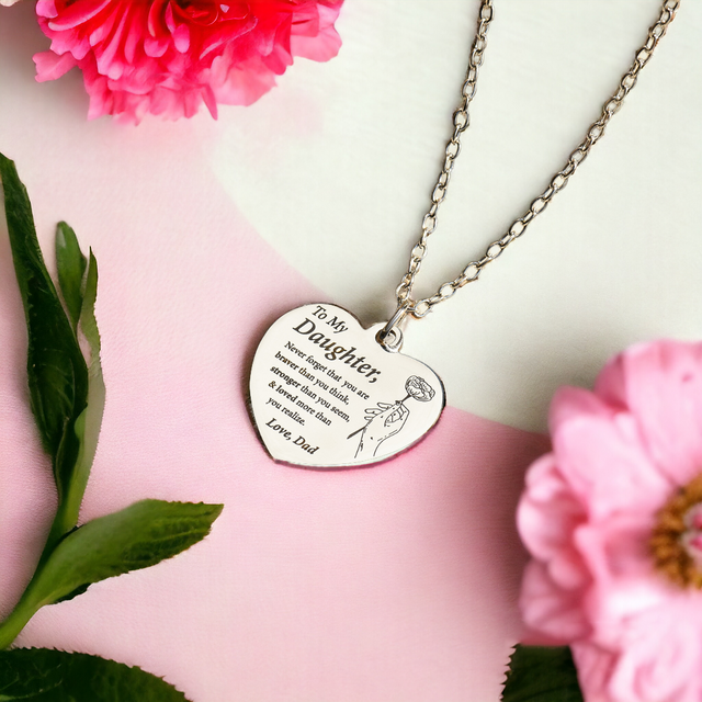 silver engraved heart necklace on white and pink canvas with flowers around it