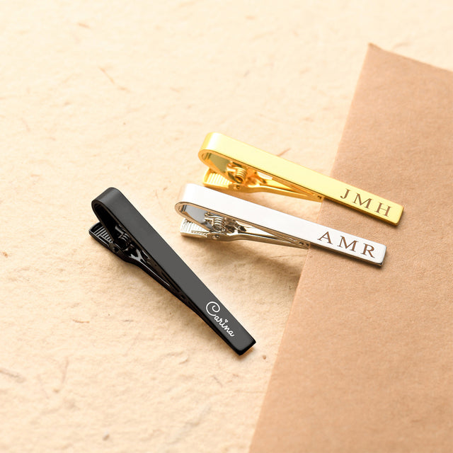 black, silver, and gold Personalized Tie Clips on sand and brown envelope