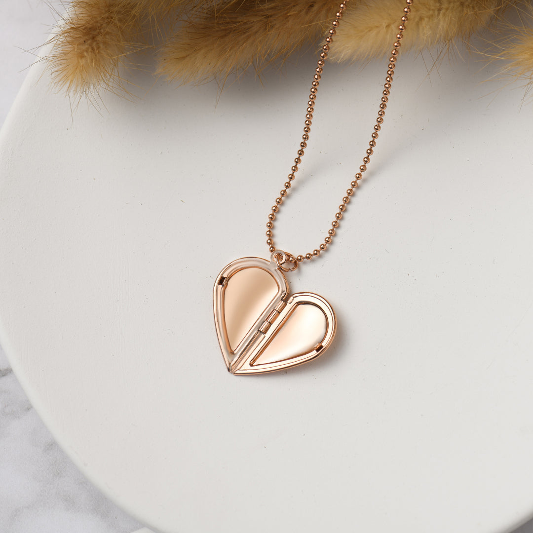 an opened rose gold colored Couple's Heart Locket Necklace on top of a white circle disc